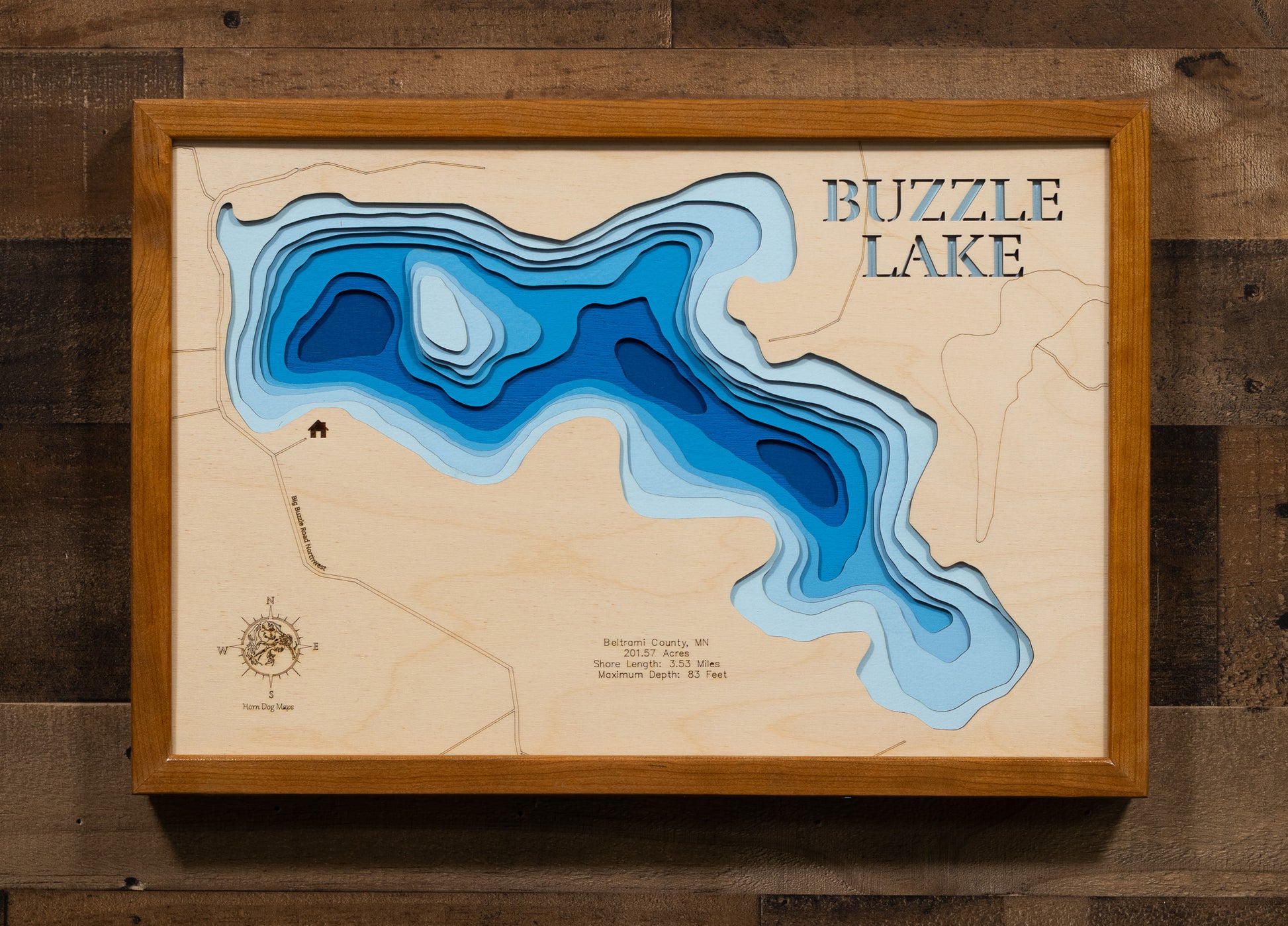 A laser-cut, layered wooden map of Buzzle Lake in Beltrami County, Minnesota. The shape of the lake is clearly defined within the northern Minnesota landscape. The varying depths of the lake, reaching a maximum of 83 feet, are represented by different layers of wood.