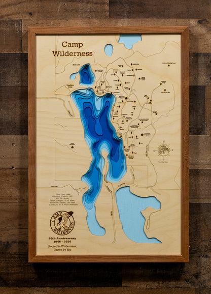 A framed 3D wooden topographic map of Camp Wilderness, featuring layered blue and light blue resin cutouts representing lakes and water features, mounted on a rustic dark wood plank wall.