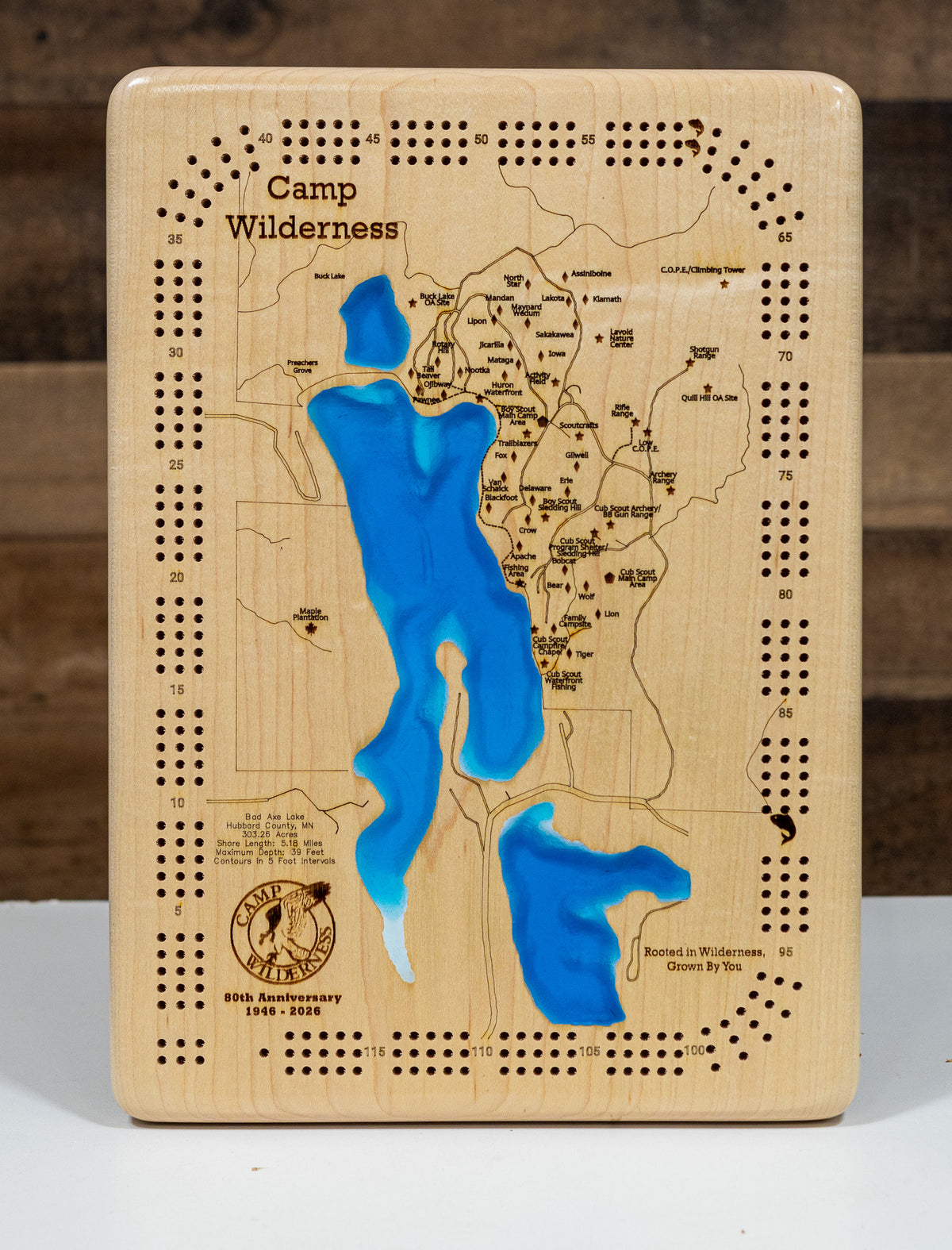 A Cribbage Board titled 'Camp Wilderness' featuring an engraved map with blue recessed water features, photographed against a dark wood background.