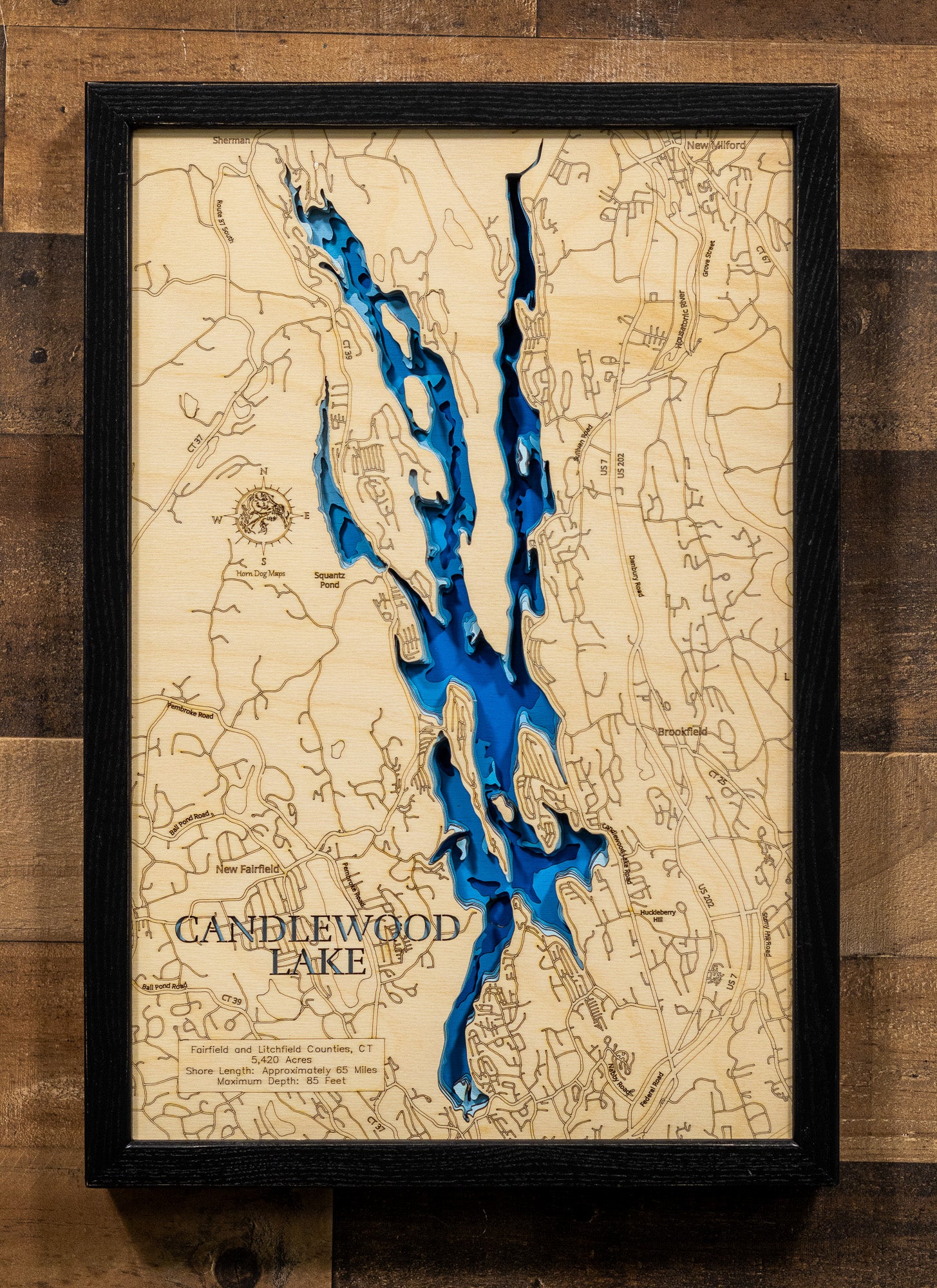A laser-cut, layered wood map of Candlewood Lake, Connecticut, highlighting its winding shoreline and surrounding wooded areas.