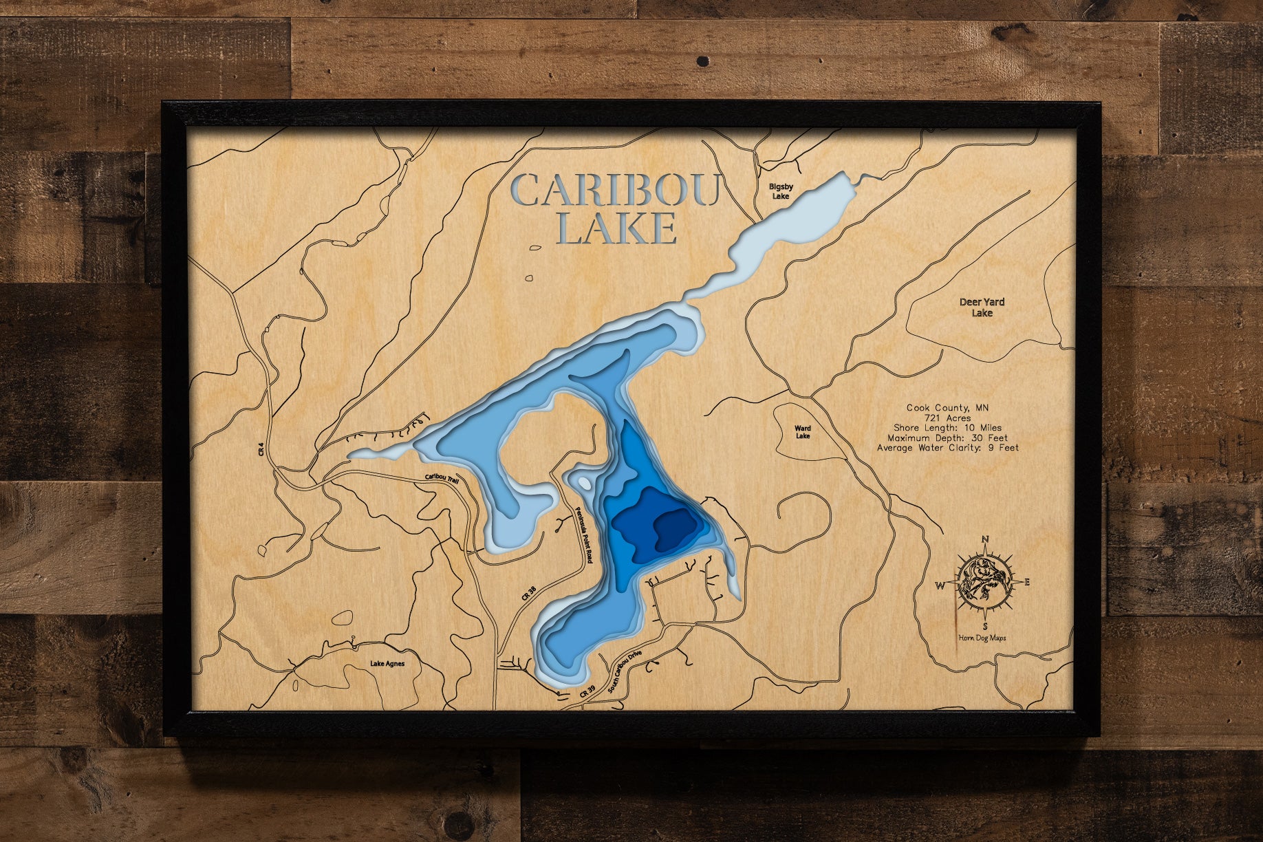 A meticulously detailed, laser-cut, multi-layered wooden map of Caribou Lake in Cook County, Minnesota, showcasing the 721-acre lake with 10 miles of shoreline nestled in the Sawtooth Mountains near Lutsen. The topographic design features natural wood layers highlighting the surrounding Superior National Forest and graduated blue water layers illustrating depths to the 30-foot maximum.