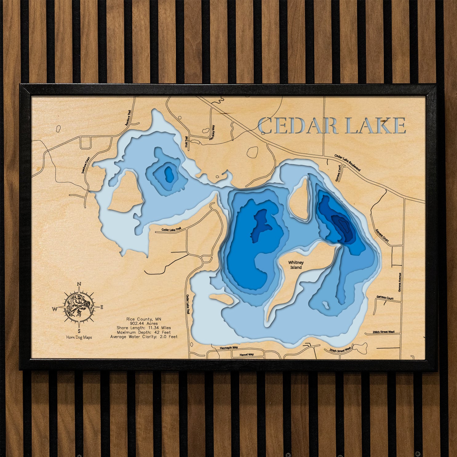 A precision laser-cut, multi-layered wooden map of Cedar Lake in Rice County, Minnesota. The natural wood top layer captures over 11 miles of shoreline and four distinctive islands in fine detail, while a light-to-dark blue gradient conveys the lake's 42-foot depth. A handcrafted statement piece for any southern Minnesota lake home, cabin, or fishing enthusiast's wall.