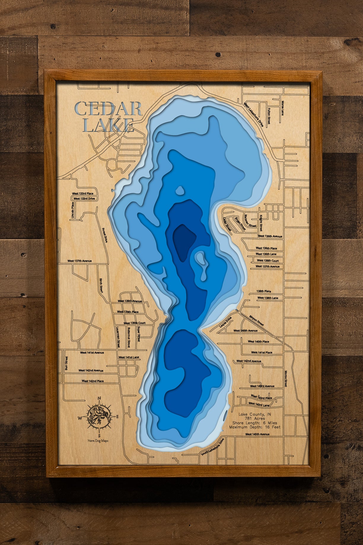 A meticulously detailed, laser-cut, multi-layered wooden topographical map of Cedar Lake in Lake County, Indiana, showcasing Northwest Indiana's largest natural lake at 781 acres measuring 2.1 miles long with depth contours from the 8.8-foot median to the 16-foot maximum in the middle basin. The natural wood top layer frames six miles of shoreline with the public access and historic Valparaiso Moraine hills, while graduated blue layers create a gentle visual depth gradient.