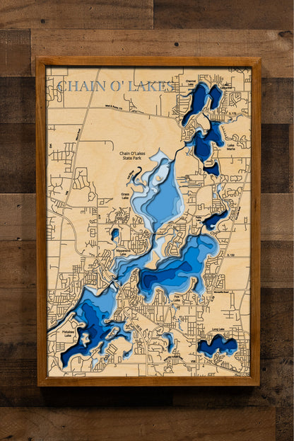 A laser-cut, layered wooden map of the Chain O'Lakes, located in McHenry and Lake Counties, Illinois. The interconnected and intricate shapes of the 15 lakes and connecting waterways are clearly visible within the northeastern Illinois landscape. The varying depths of the individual lakes are represented by different layers of wood, illustrating the underwater topography of this unique system.