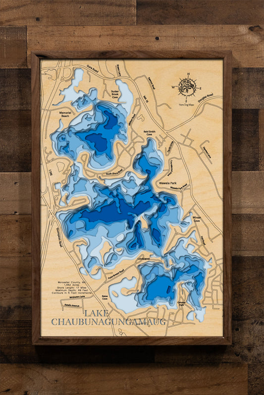 A laser-cut, layered wooden map of Lake Chaubunagungamaug in Worcester County, Massachusetts. The shape of the lake, with its interesting bays and features, is clearly visible within the south-central Massachusetts landscape. The varying depths of the lake, reaching a maximum of 49 feet, are represented by different layers of wood.
