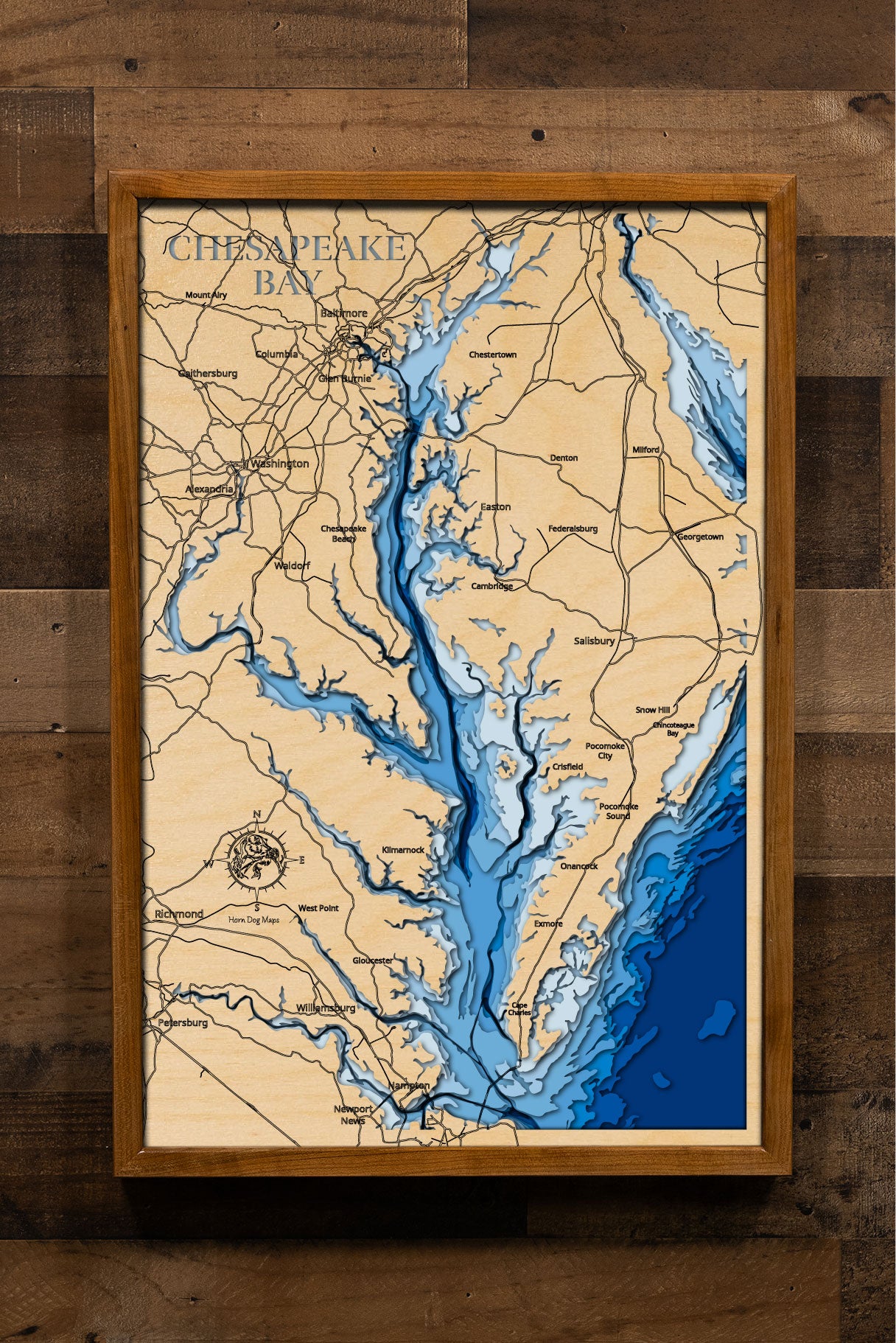 A laser-cut, layered wooden map of the Chesapeake Bay, located in Maryland, Virginia, and Delaware. The expansive and intricate shape of this major estuary, with its numerous tributaries and coastline, is clearly visible within the Mid-Atlantic landscape. The varying depths of the bay, reaching a maximum of 174 feet, are represented by different layers of wood, illustrating its underwater topography.