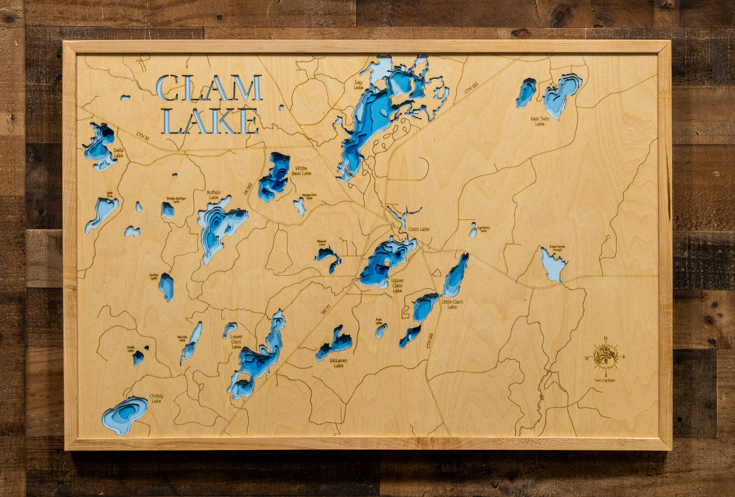 A magnificently detailed, laser-cut, multi-layered wooden topographical map of the Clam Lake area lakes in Ashland and Sawyer Counties, Wisconsin, showcasing the interconnected chain of Upper Clam, Lower Clam, White Bass, Day, and surrounding lakes with intricate shorelines winding through the Chequamegon National Forest. The natural wood top layer frames the pristine wilderness character and elk habitat, while graduated blue layers create a stunning visual depth gradient across this premier northwoods fish