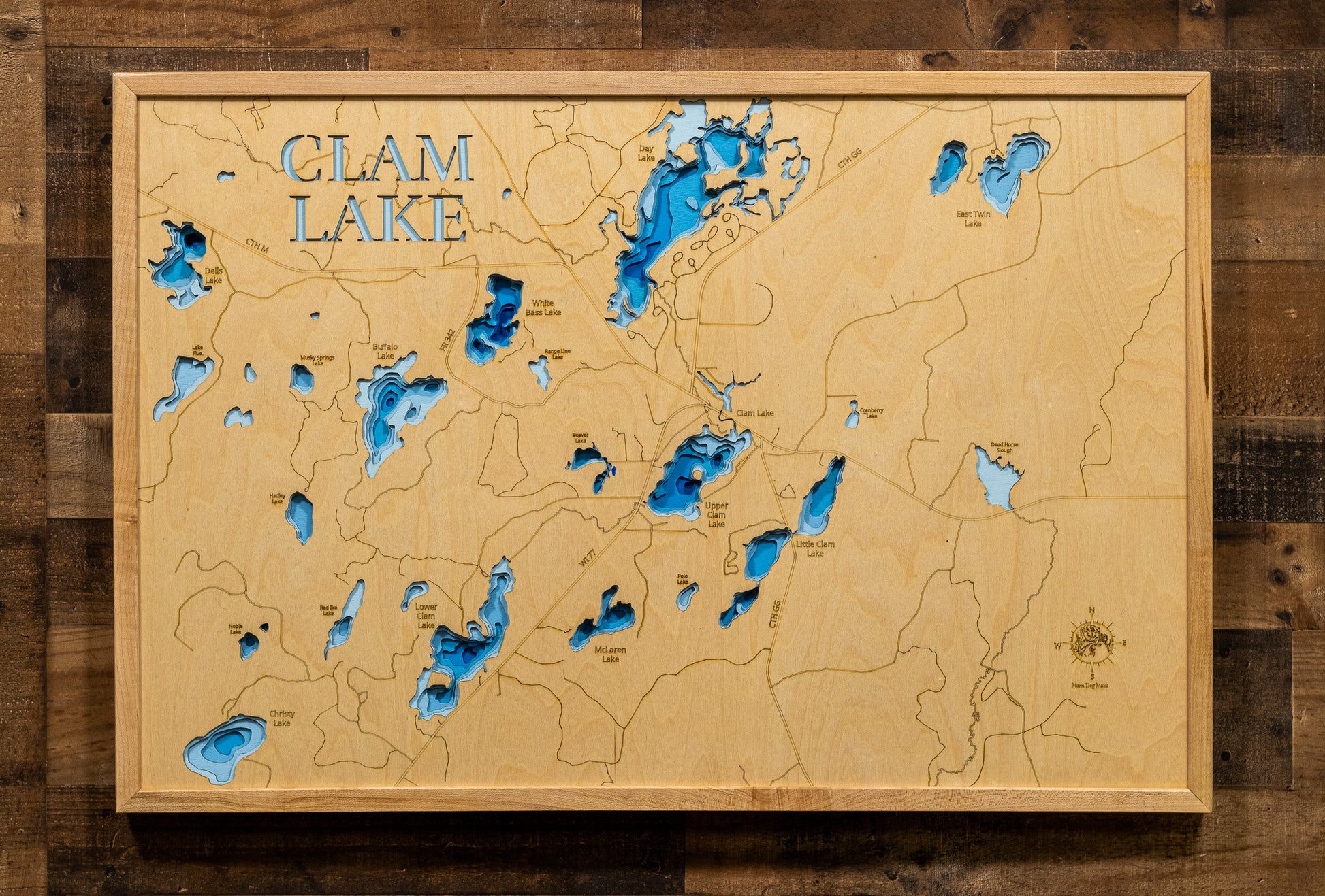 A magnificently detailed, laser-cut, multi-layered wooden topographical map of the Clam Lake area lakes in Ashland and Sawyer Counties, Wisconsin, showcasing the interconnected chain of Upper Clam, Lower Clam, White Bass, Day, and surrounding lakes with intricate shorelines winding through the Chequamegon National Forest. The natural wood top layer frames the pristine wilderness character and elk habitat, while graduated blue layers create a stunning visual depth gradient across this premier northwoods fish