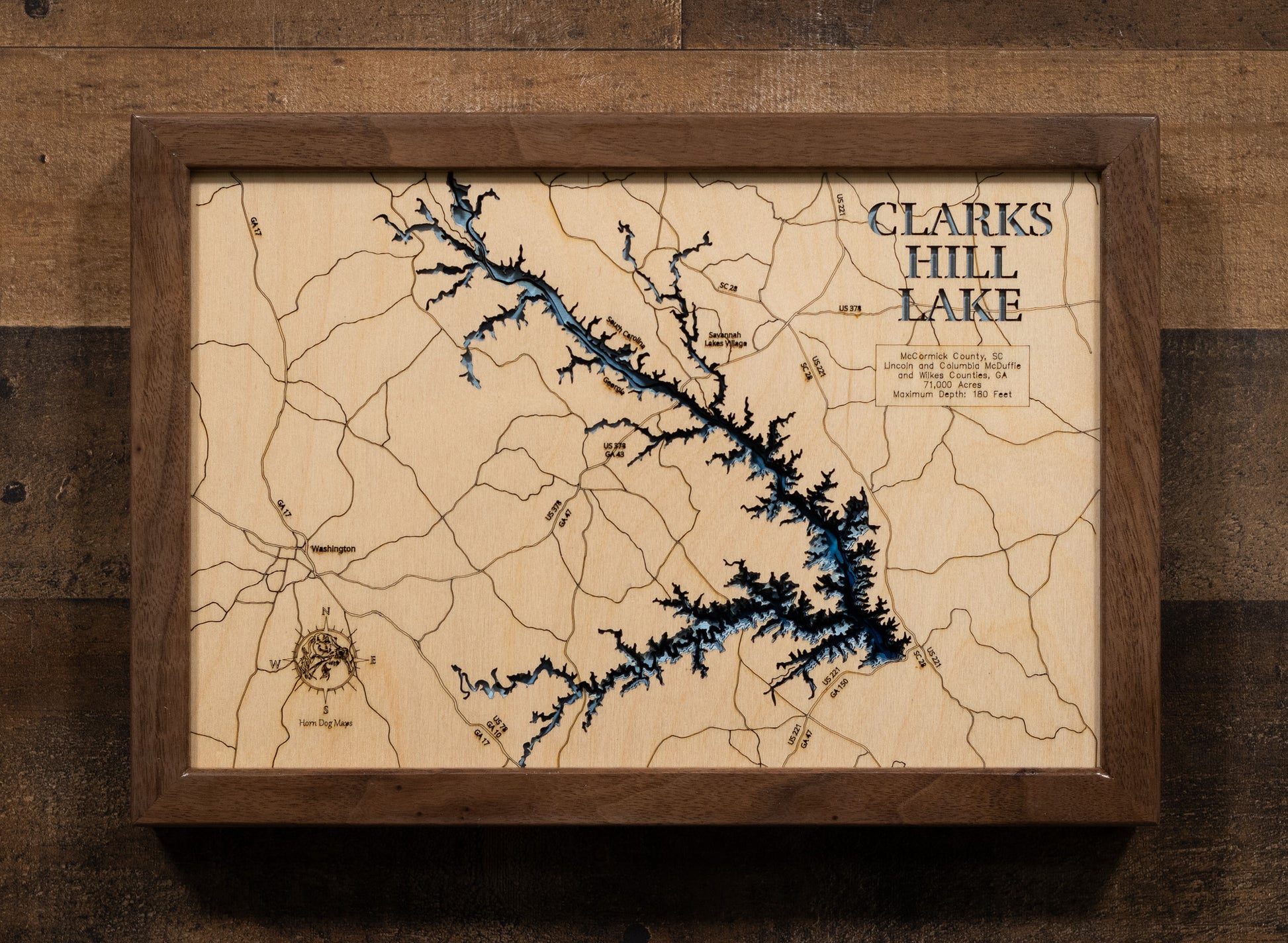 A laser-cut, layered wooden map of Clarks Hill Lake, located in Columbia, Elbert, Lincoln, and McDuffie Counties, Georgia. The expansive and intricate shape of the reservoir, stretching along the Savannah River, is clearly visible within the eastern Georgia landscape. The varying depths of the lake, reaching a maximum of 180 feet, are represented by different layers of wood, illustrating its underwater topography.