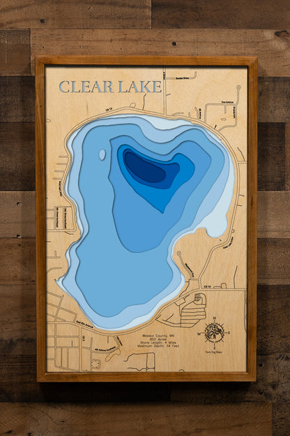A detailed, laser-cut, multi-layered wooden map of Clear Lake in Waseca County, Minnesota, showcasing the 652-acre lake with 4 miles of shoreline right within the town of Waseca. The topographic design features natural wood layers highlighting the two public accesses and surrounding agricultural landscape, with graduated blue water layers illustrating depths to the 34-foot maximum.