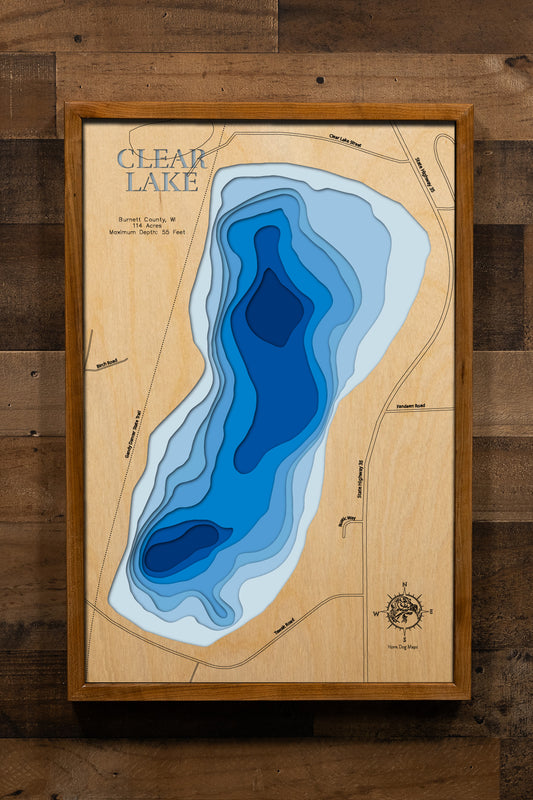 A detailed, laser-cut, multi-layered wooden map of Clear Lake in Burnett County, Wisconsin, showcasing the 114-acre lake with moderately clear waters near Siren. The topographic design features natural wood layers highlighting the sandy bottom and surrounding forest landscape, with graduated blue water layers illustrating depths to the 55-foot maximum.