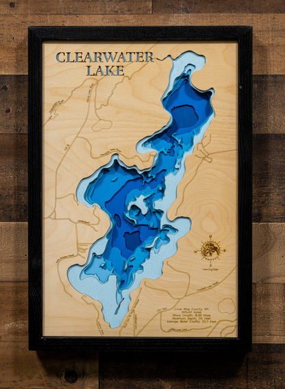A framed wooden depth map of Clearwater Lake, featuring layered blue and light blue wood sections representing water depth, with contour lines and a black frame, mounted on a rustic dark wood plank wall.