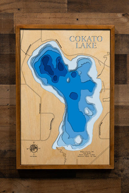 A precision laser-cut, multi-layered wooden map of Cokato Lake in Wright County, Minnesota, a 539-acre lake northeast of Cokato with a rich and diverse fishery managed actively for Walleye. The natural wood top layer captures 5 miles of shoreline in fine detail, while a light-to-dark blue gradient conveys the lake's 52-foot depth. A handcrafted statement piece for any Minnesota lake home, cabin, or outdoor enthusiast's wall.