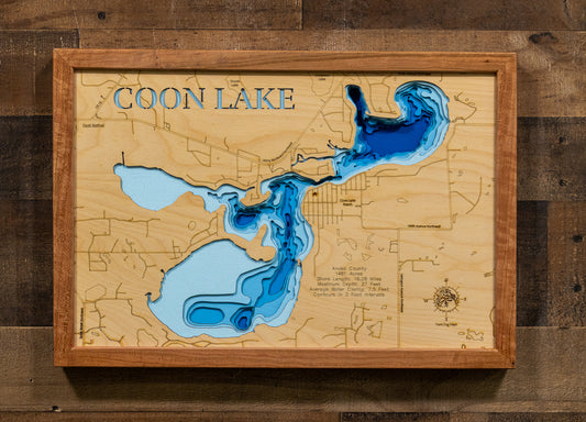 A framed wooden Coon Lake depth map wall art piece, featuring blue resin filled low points and a light wood background, mounted on a dark wood plank wall.