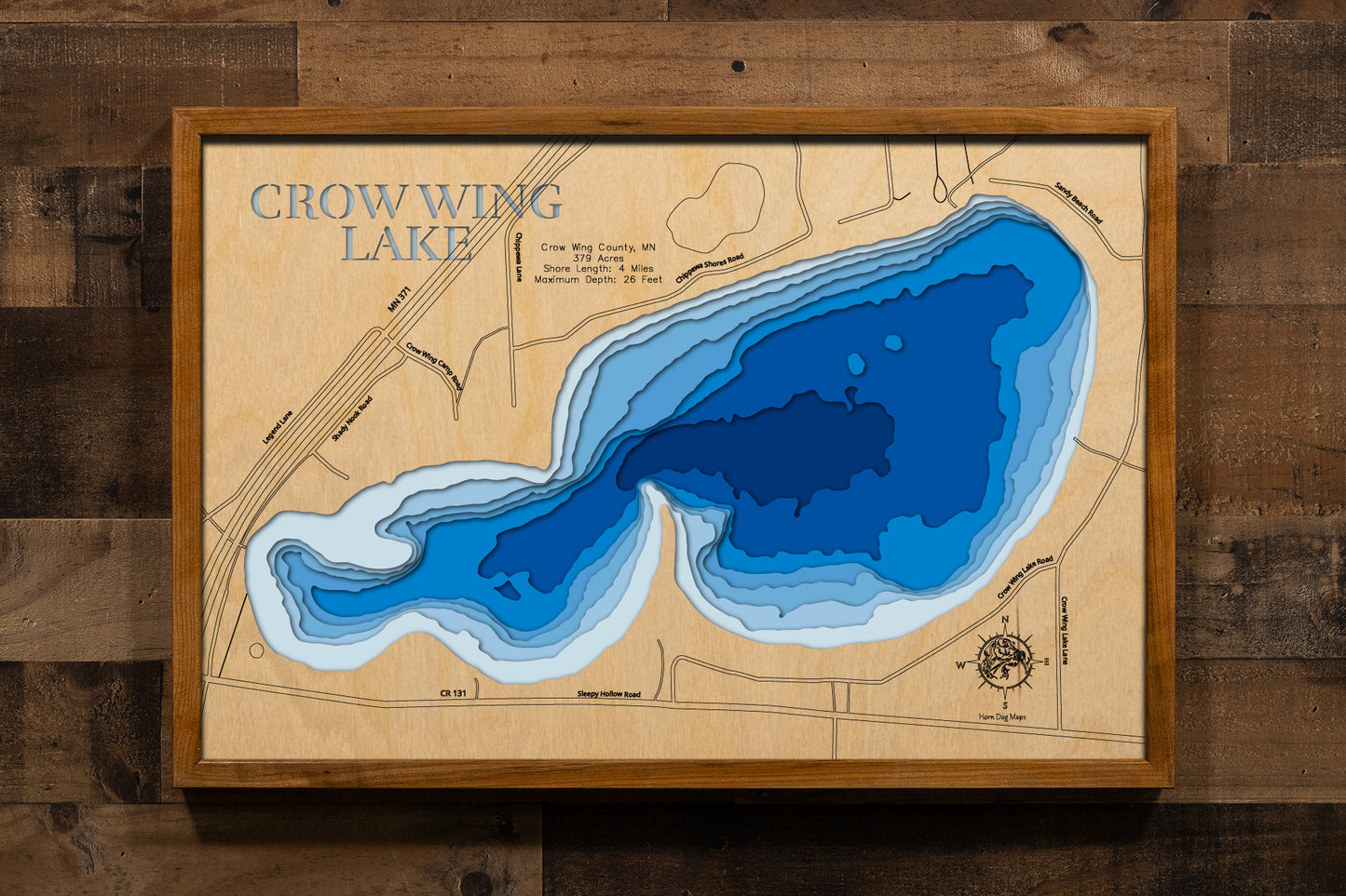 A meticulously detailed, laser-cut, multi-layered wooden topographical map of Crow Wing Lake in Crow Wing County, Minnesota, showcasing the 379-acre shallow, fertile lake with depth contours from the 11-foot average depth to the 26-foot maximum. The natural wood top layer frames four miles of shoreline with aquatic vegetation and the public boat launch, while graduated blue layers create a gentle visual depth gradient.
