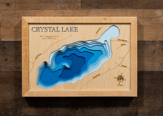 A laser-cut, layered wooden map of Crystal Lake in Forest and Langlade Counties, Wisconsin. The distinct shape of this natural lake, with its 75-acre surface, is clearly visible within the forested landscape of northern Wisconsin. The varying depths of the lake, reaching a maximum of 36 feet, are represented by different layers of wood, illustrating its underwater topography.
