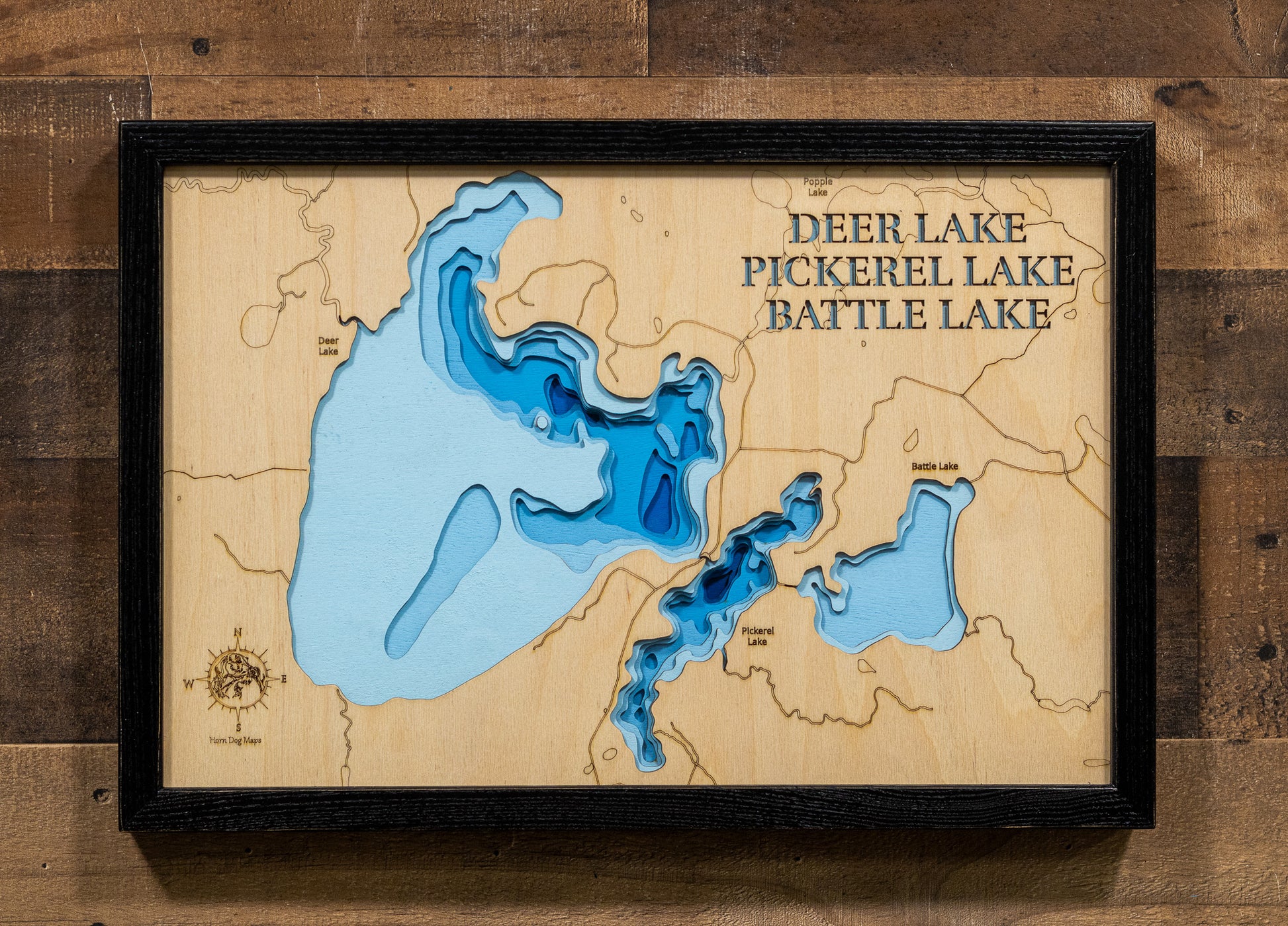 A precision laser-cut, multi-layered wooden map of the Deer, Pickerel, and Battle Lake chain in Itasca County, Minnesota. The natural wood top layer captures the interconnected shorelines of all three lakes — including Deer Lake's 25 islands — in fine detail, while a light-to-dark blue gradient highlights their dramatically varying depths. A distinctive, rustic statement piece for any Minnesota Northwoods cabin or lake home.