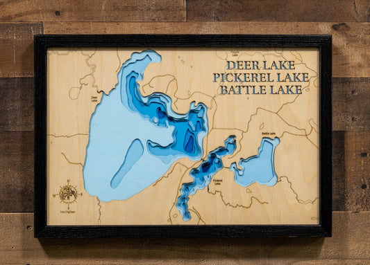 A precision laser-cut, multi-layered wooden map of the Deer, Pickerel, and Battle Lake chain in Itasca County, Minnesota. The natural wood top layer captures the interconnected shorelines of all three lakes — including Deer Lake's 25 islands — in fine detail, while a light-to-dark blue gradient highlights their dramatically varying depths. A distinctive, rustic statement piece for any Minnesota Northwoods cabin or lake home.