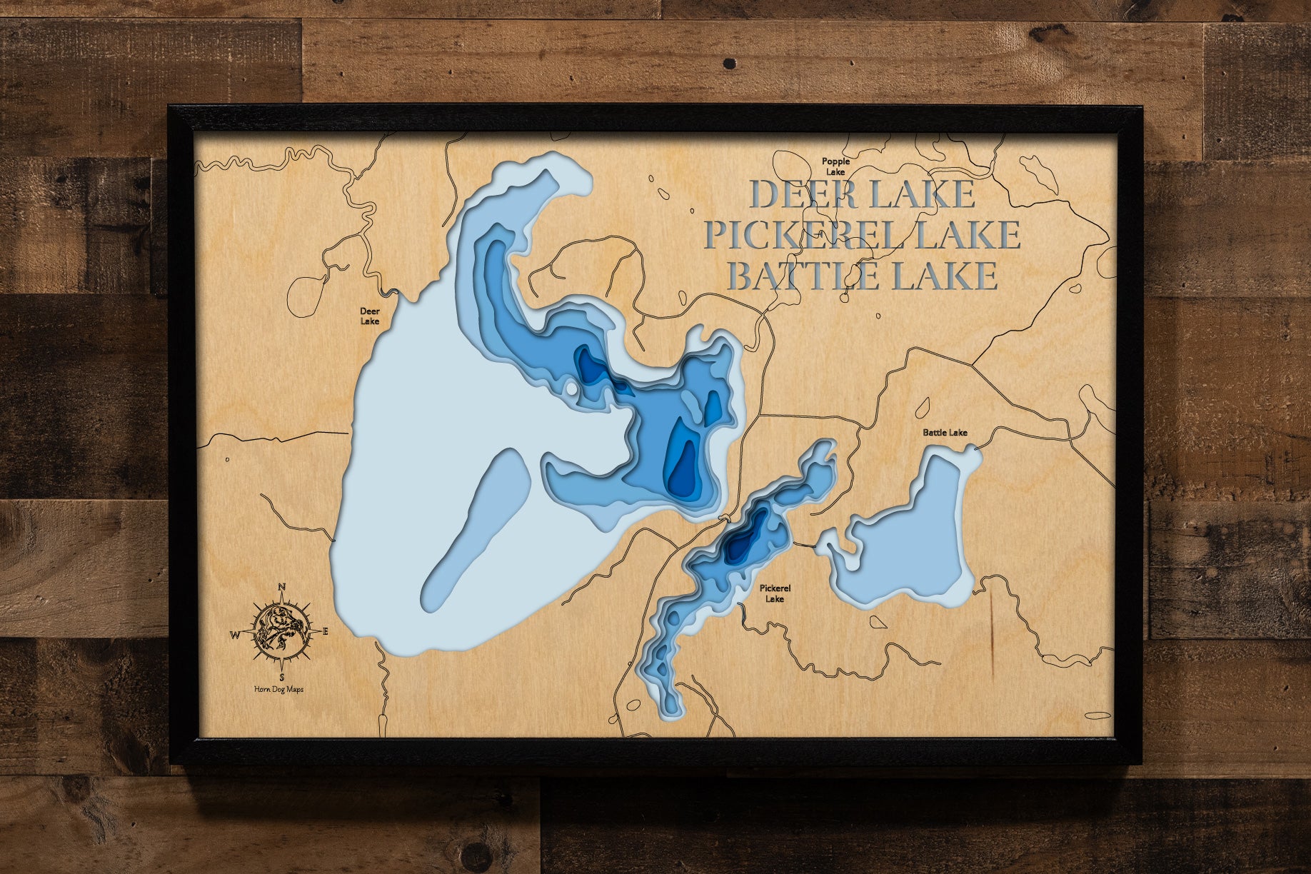 A precision laser-cut, multi-layered wooden map of the Deer, Pickerel, and Battle Lake chain in Itasca County, Minnesota. The natural wood top layer captures the interconnected shorelines of all three lakes — including Deer Lake's 25 islands — in fine detail, while a light-to-dark blue gradient highlights their dramatically varying depths. A distinctive, rustic statement piece for any Minnesota Northwoods cabin or lake home.