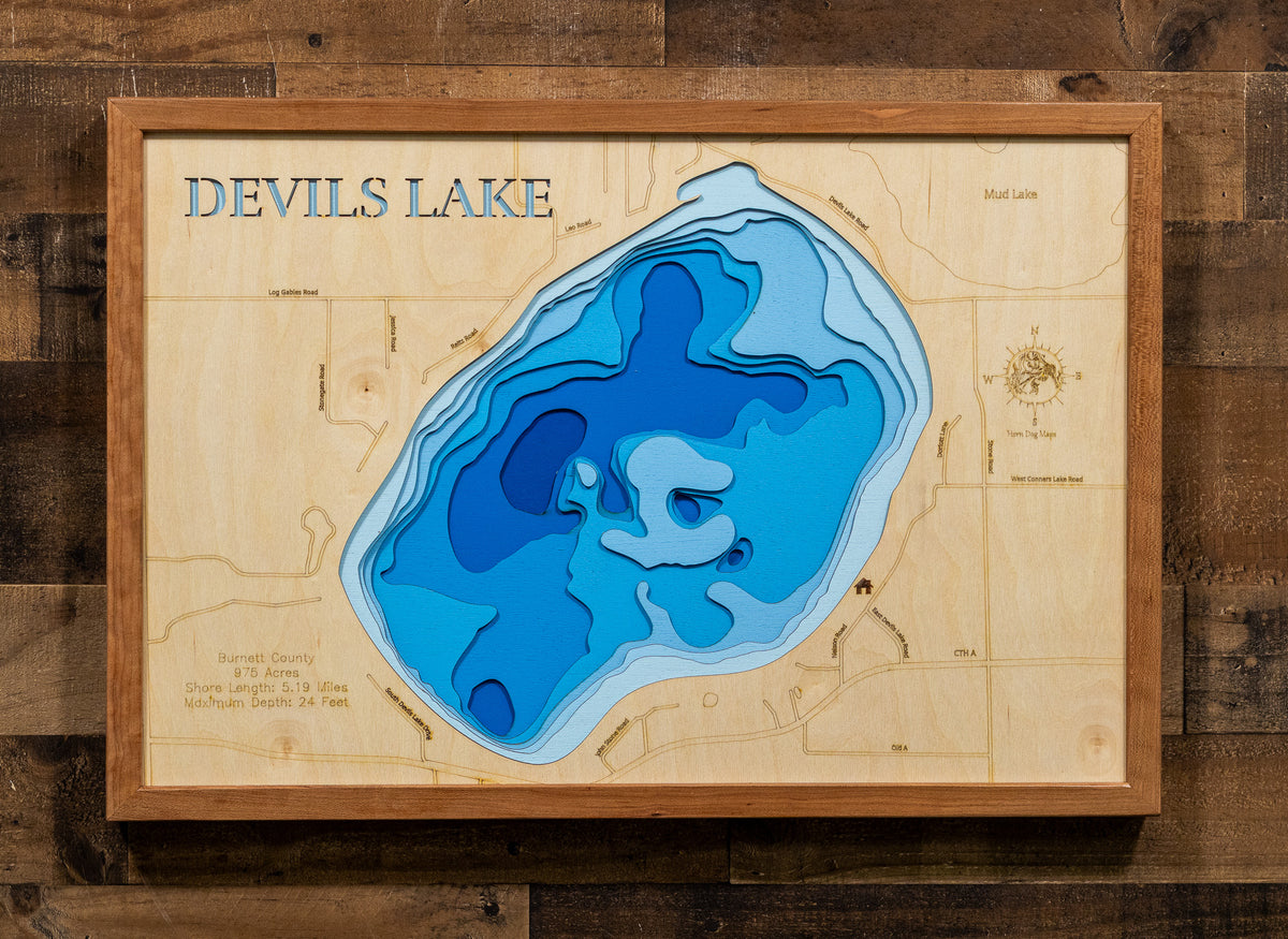 A framed wooden depth map of Devils Lake, featuring layered blue and cyan water contours on a light natural wood background, mounted on a dark wood plank wall.