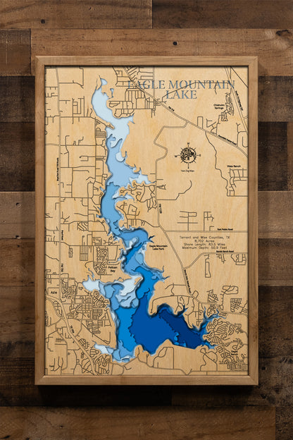 A precision laser-cut, multi-layered wooden map of Eagle Mountain Lake in Tarrant and Wise Counties, Texas. The natural wood top layer captures 83.5 miles of winding reservoir shoreline in fine detail, while a light-to-dark blue gradient highlights the lake's depth of nearly 51 feet. A striking, handcrafted statement piece for any Texas lake home, ranch house, or outdoor enthusiast's wall.