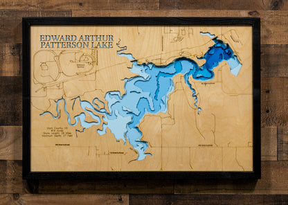 A framed 3D wooden cutout map of Edward Arthur Patterson Lake, featuring layered blue and light blue wood sections representing the lake's depth, mounted on a rustic dark wood plank wall.