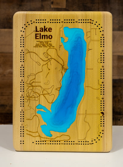 A highly detailed, laser-cut, and multi-layered wooden map of Lake Elmo, a natural lake in Washington County, Minnesota. The map shows the lake's distinct shape, its shoreline of 3.31 miles, and its central location within Lake Elmo Park Reserve. The varying depths of the lake, reaching a maximum of 44 feet, are represented by different layers of wood.