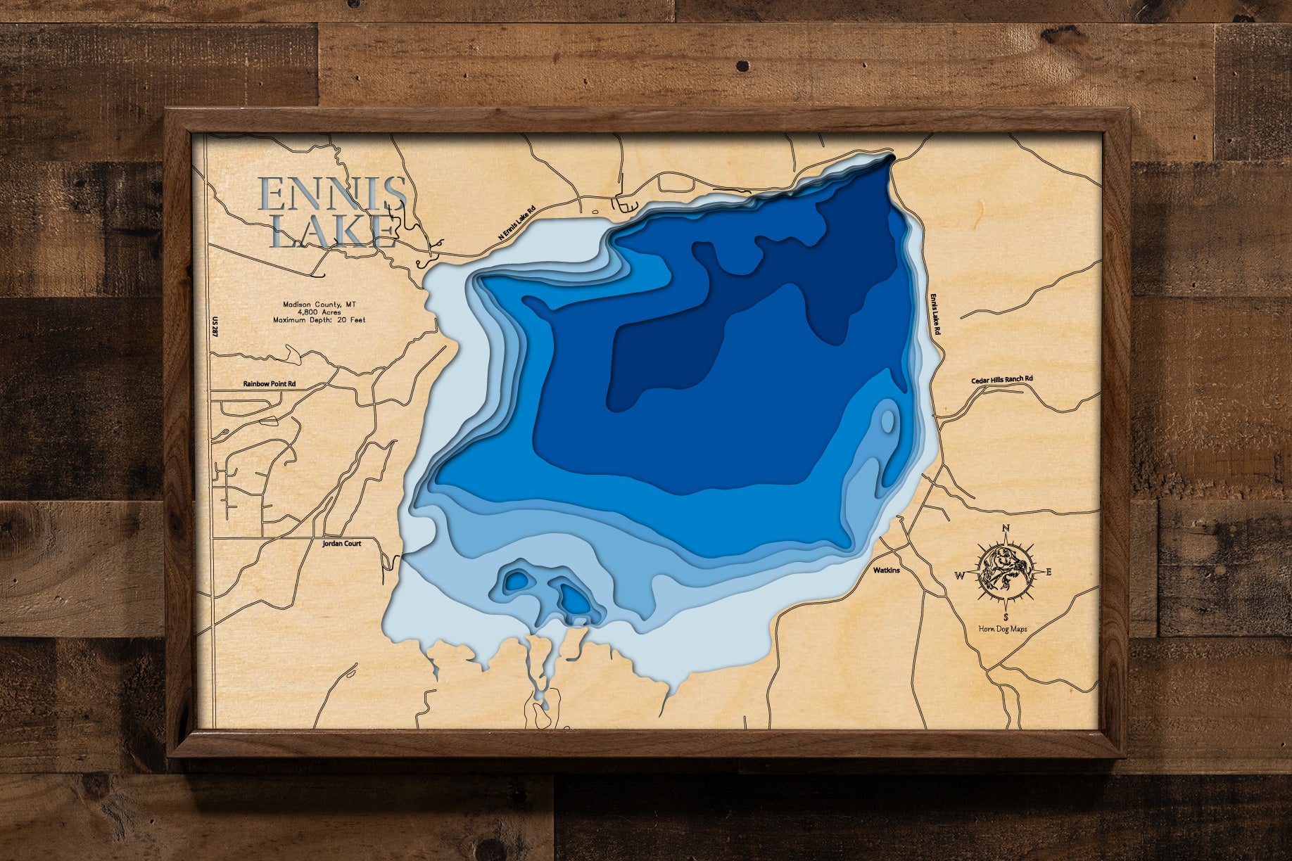 A highly detailed, laser-cut, and multi-layered wooden map of Ennis Lake, a reservoir in Madison County, Montana. The map shows the lake's distinct shape and its location on the Madison River. The varying depths of the lake, reaching a maximum of 20 feet, are represented by different layers of wood, illustrating its impressive underwater topography.