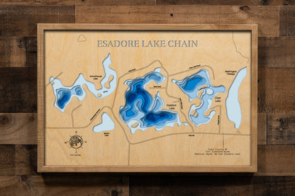 A precision laser-cut, multi-layered wooden map of the Esadore Lake Chain — Esadore, Schoolhouse, Clear, Martin, and Washington Flowage — in Taylor County, Wisconsin. The natural wood top layer details the intimate, interconnected shorelines of all five lakes, while a light-to-dark blue gradient highlights depth and dimension. A distinctive rustic statement piece perfect for a cabin, lodge, or Northwoods-inspired space.