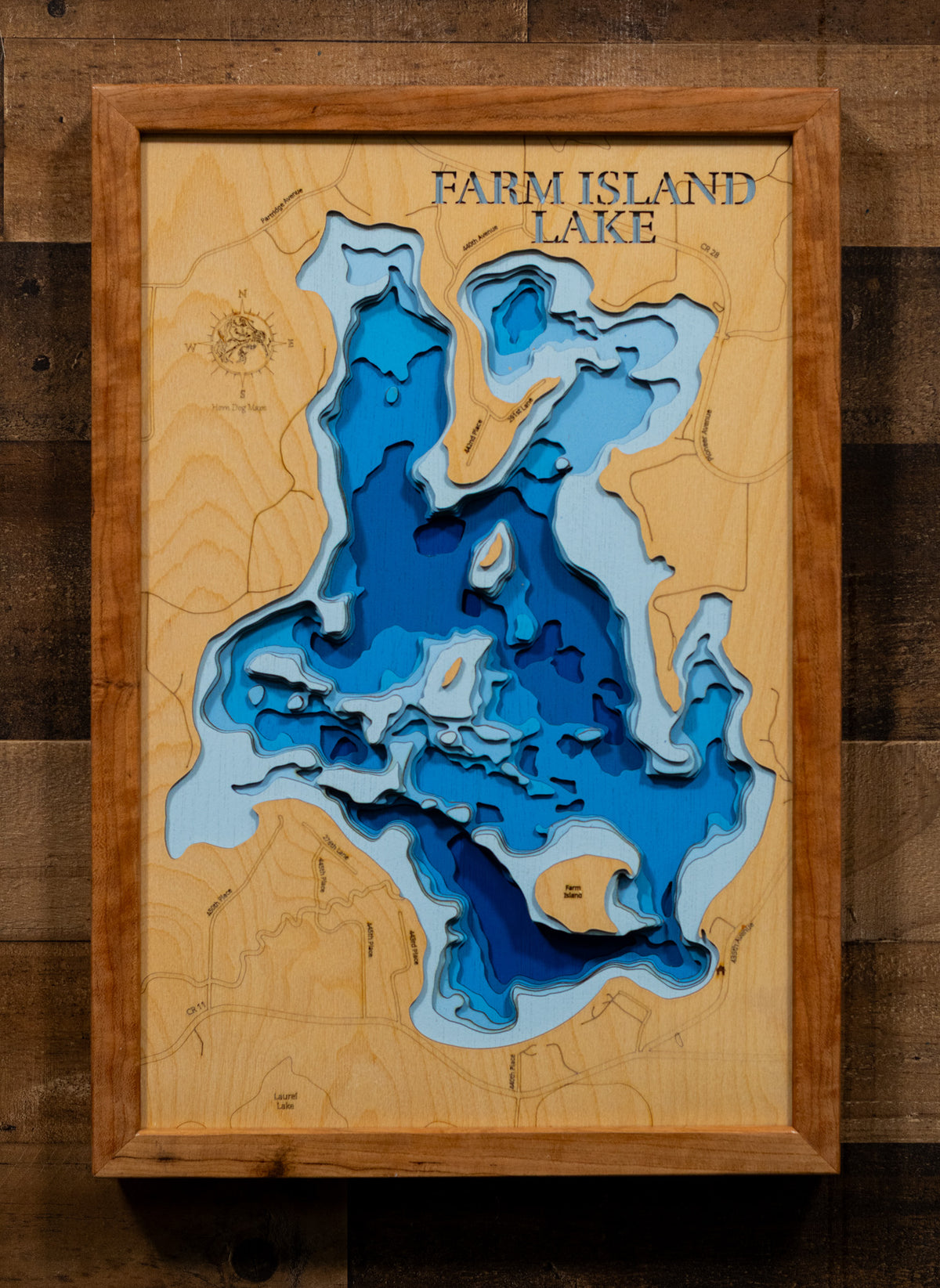 A 3D layered wooden map of Farm Island Lake, featuring layered blue and light blue depths on a natural wood background, mounted on a rustic dark wood plank wall.
