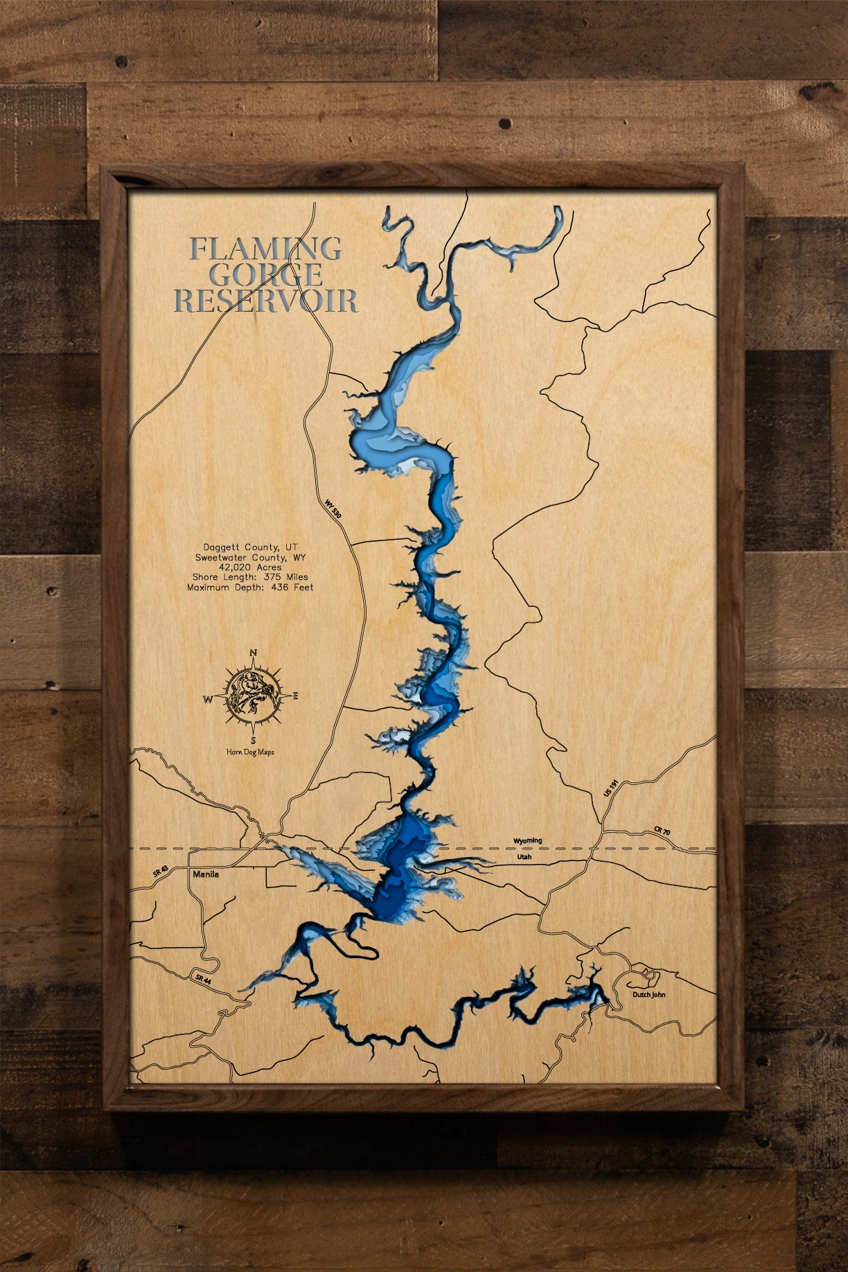 A masterfully crafted, multi-layered laser-cut wooden topographic map of Flaming Gorge Reservoir spanning the Utah-Wyoming border across Daggett and Sweetwater Counties, featuring intricate depth contours illustrating the dramatic 436-foot maximum depth, the winding 91-mile serpentine course from the dam through narrow red rock canyons to wide Wyoming badlands, the extensive 375-mile shoreline with countless coves and inlets, prominent landmarks including Red Canyon, Hideout Canyon, Sheep Creek Bay, the thr