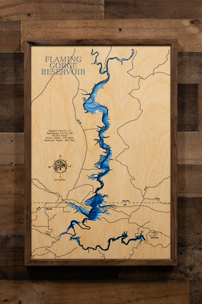 A masterfully crafted, multi-layered laser-cut wooden topographic map of Flaming Gorge Reservoir spanning the Utah-Wyoming border across Daggett and Sweetwater Counties, featuring intricate depth contours illustrating the dramatic 436-foot maximum depth, the winding 91-mile serpentine course from the dam through narrow red rock canyons to wide Wyoming badlands, the extensive 375-mile shoreline with countless coves and inlets, prominent landmarks including Red Canyon, Hideout Canyon, Sheep Creek Bay, the thr