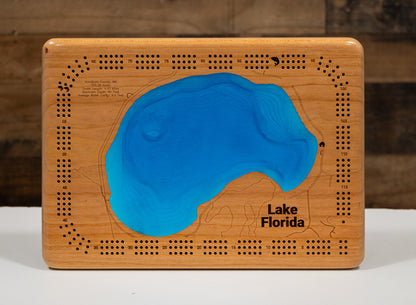 A rectangular wooden plaque featuring an embossed map design with a bright blue resin-filled shape representing Lake Florida, shown on a white surface against a dark wood background.