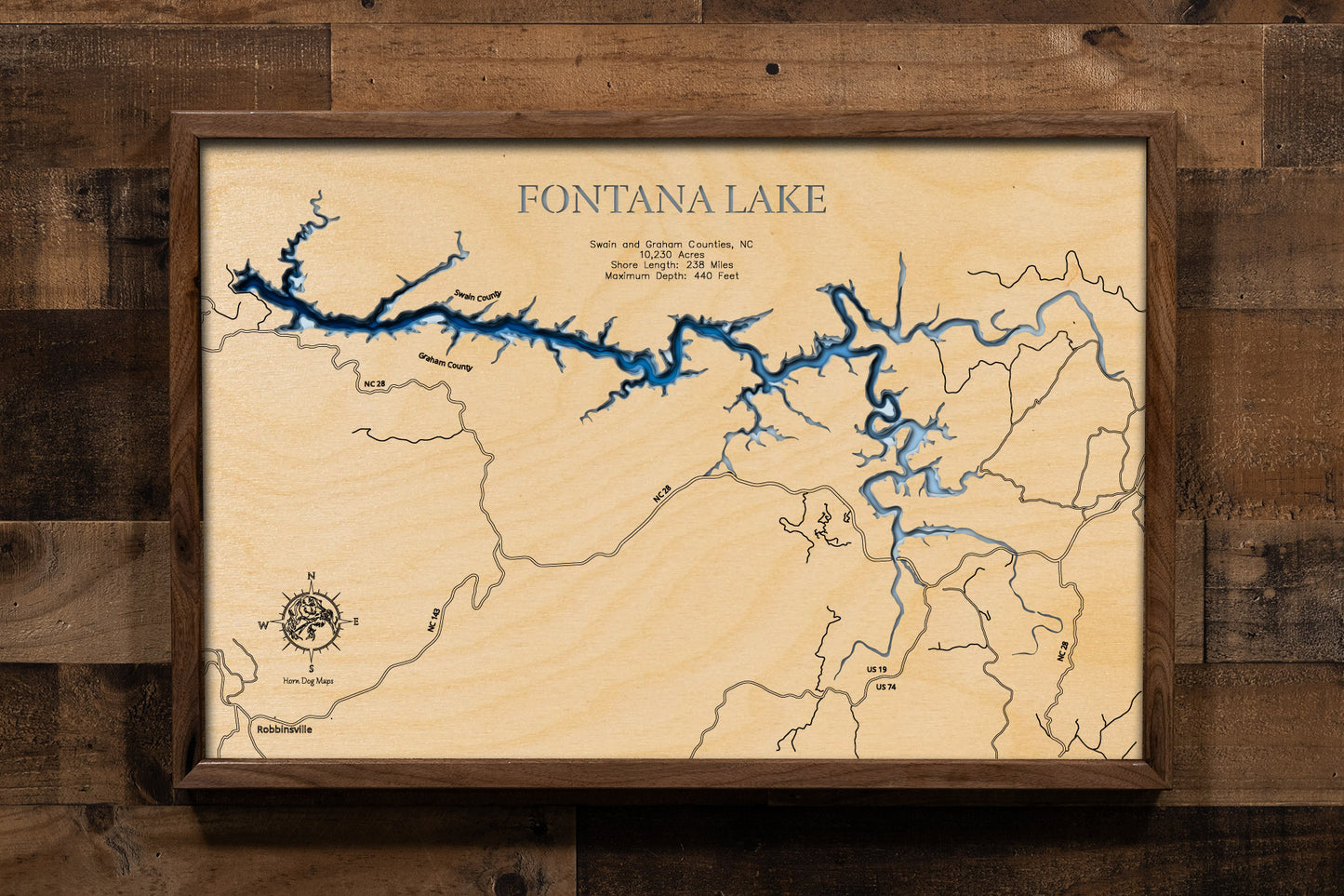 A laser-cut, layered wooden map of Fontana Lake in North Carolina. The distinct, elongated, and winding shape of this large reservoir, with its numerous arms and 238-mile shoreline, is clearly visible as it stretches through Swain and Graham Counties, bordering national park and forest lands. The varying depths of the lake, reaching a maximum of 440 feet, are represented by different layers of wood, illustrating its impressive underwater topography.