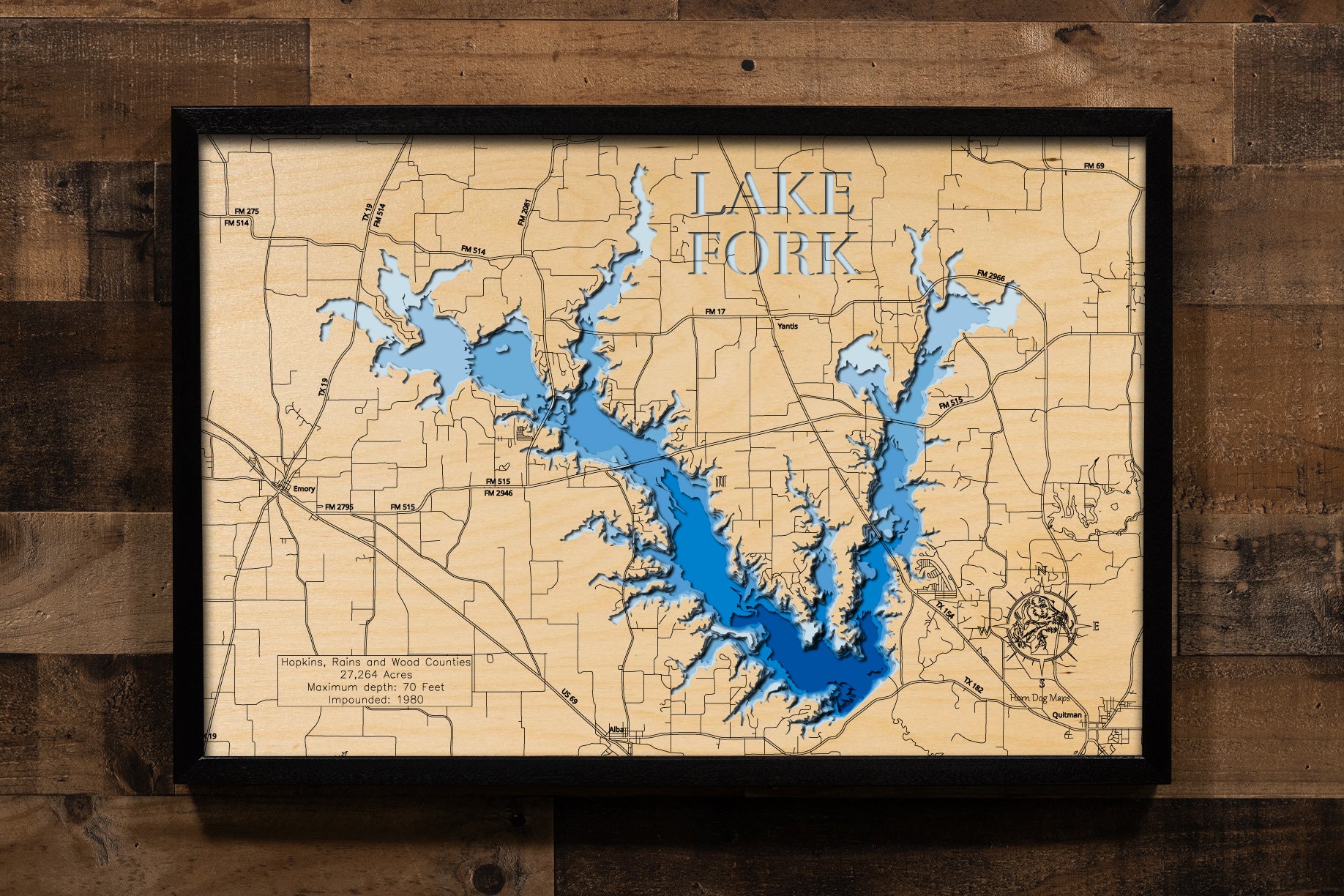 A highly detailed, 3D laser-cut wooden map of Lake Fork in Wood County, Texas. The multi-layered design uses different wood tones to illustrate the lake's bathymetric contours and deepest points. Etched details include the lake name, county lines, submerged timber, and surrounding roads, creating a unique and intricate piece of art.