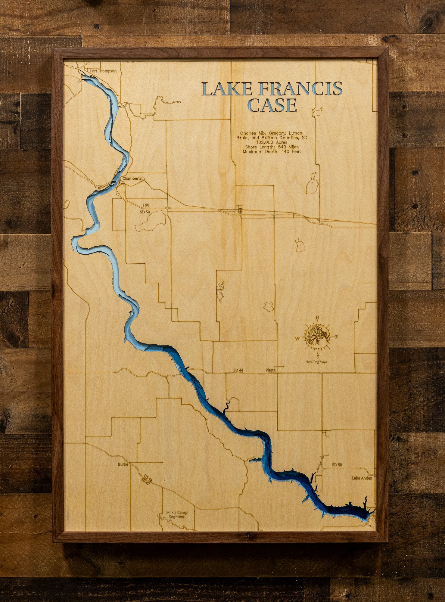 A framed wooden map of Lake Francis Case, featuring a light natural wood background, engraved county lines, and a winding blue lake representation, mounted on a rustic dark wood plank wall.