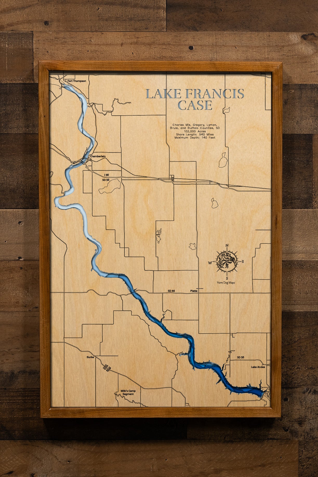 An intricately detailed, multi-layered laser-cut wooden topographic map of Lake Francis Case spanning five South Dakota counties, illustrating the reservoir's impressive 107-mile serpentine course along the Missouri River, depth contours showing the 140-foot maximum depth, the extensive 540-mile shoreline with countless coves and creek arms, Fort Randall Dam at the southern terminus, and major landmarks including Chamberlain, the White River confluence, and Big Bend Dam.
