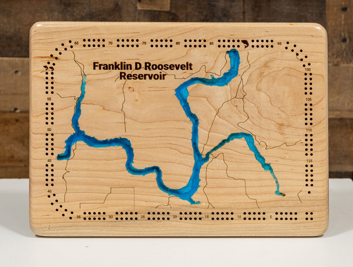 A precision laser-cut, multi-layered wooden map of Franklin D. Roosevelt Lake spanning five counties in northeastern Washington State. The natural wood top layer captures 600 miles of dramatic Columbia River reservoir shoreline in extraordinary detail, while a light-to-dark blue gradient highlights the water's depth of 375 feet. A breathtaking, rustic statement piece for any Pacific Northwest cabin, lake home, or outdoor enthusiast's space.