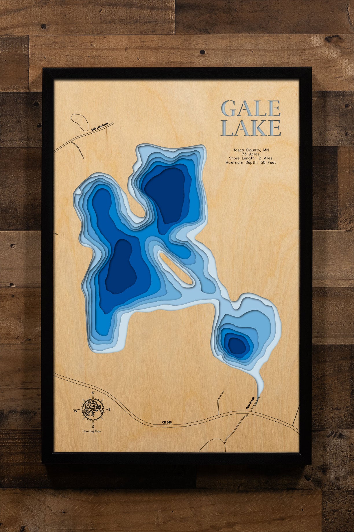 A precision laser-cut, multi-layered wooden map of Gale Lake in Itasca County, Minnesota, a secluded 73-acre lake nine miles southeast of Bigfork with no developed public access. The natural wood top layer captures 2 miles of forested shoreline in fine detail, while a light-to-dark blue gradient conveys the lake's 50-foot depth. A handcrafted statement piece for any Minnesota Northwoods cabin, lake home, or outdoor enthusiast's wall.