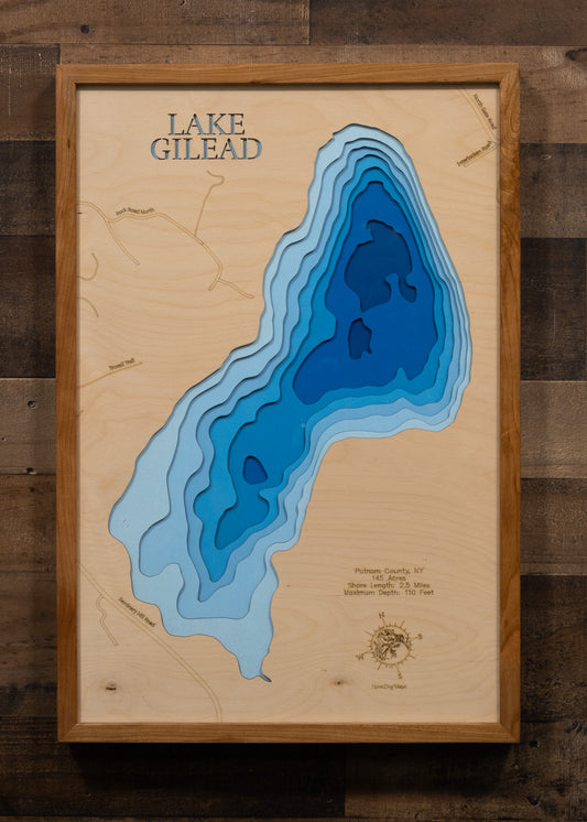 A laser-cut, layered wooden map of Lake Gilead in Putnam County, New York. The distinct shape of this natural lake, with its 2.5-mile shoreline, is clearly visible within the forested landscape of Carmel. The varying depths of the lake, reaching a maximum of 110 feet, are represented by different layers of wood, illustrating its impressive underwater topography.