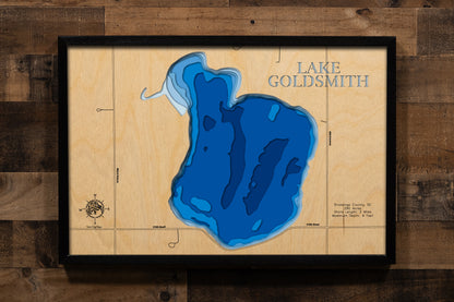 A finely crafted, laser-cut wooden lake map of Lake Goldsmith in Brookings County, South Dakota, displaying the lake's 290-acre natural basin with subtle depth contours showing the nine-foot maximum depth, the intimate two-mile shoreline with the distinctive wooded southern beach area, and the public boat launch access point near Volga.