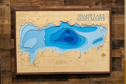 A highly detailed, 3D laser-cut wooden map of Grand Lake St. Marys in Mercer County, Ohio. The multi-layered design uses different wood tones to illustrate the lake's bathymetric contours and maximum depth. Etched details include the lake name, county lines, shoreline roads, and nearby towns like St. Marys and Celina, creating a unique and intricate piece of art.