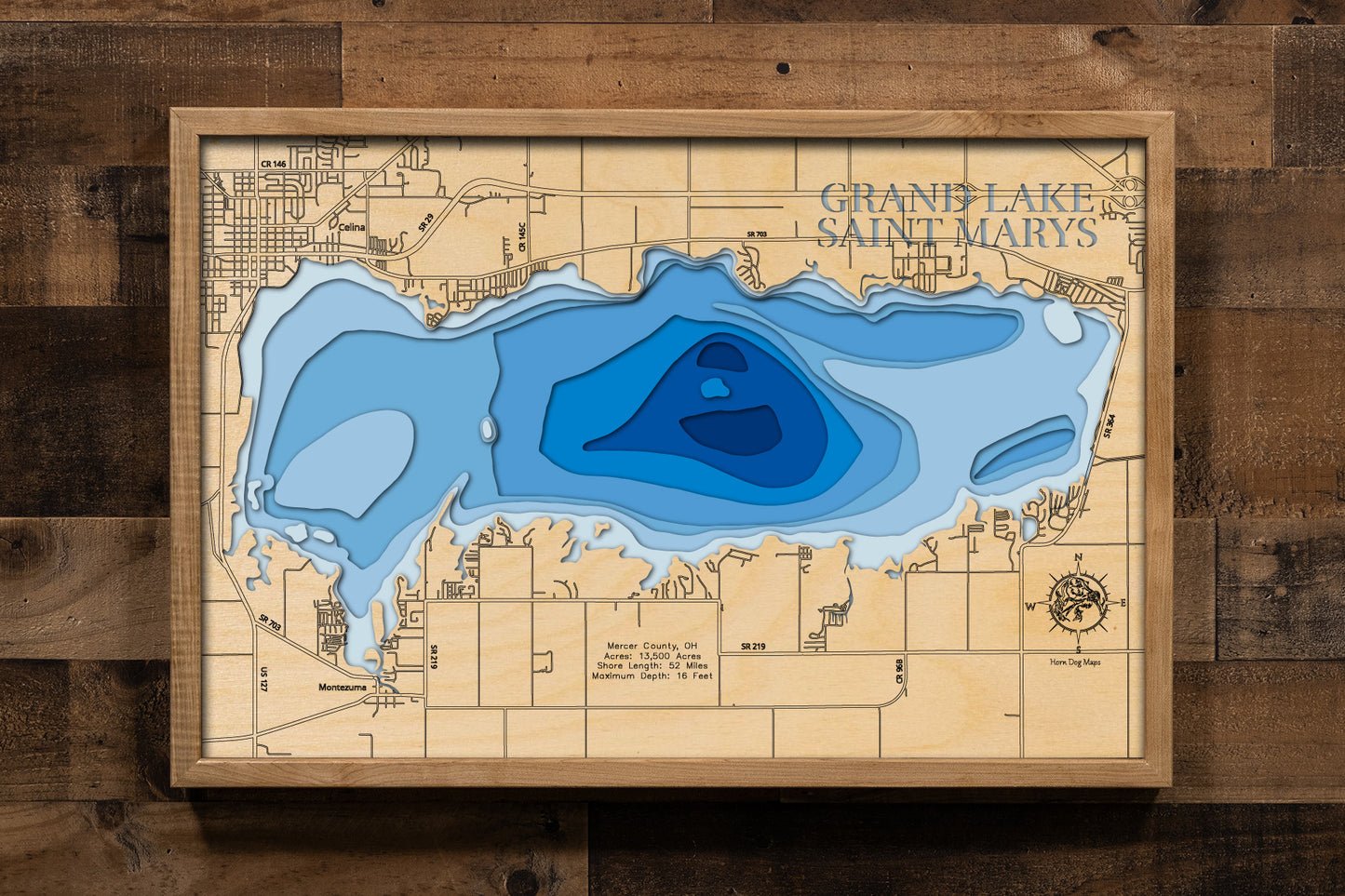 A highly detailed, 3D laser-cut wooden map of Grand Lake St. Marys in Mercer County, Ohio. The multi-layered design uses different wood tones to illustrate the lake's bathymetric contours and maximum depth. Etched details include the lake name, county lines, shoreline roads, and nearby towns like St. Marys and Celina, creating a unique and intricate piece of art.