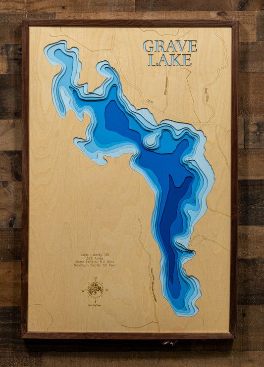 A meticulously detailed, laser-cut, multi-layered wooden topographical map of Grave Lake in Cass County, Minnesota, showcasing the 372-acre lake's irregularly shaped surface with numerous bays and points along 6.2 miles of intricate shoreline. The natural wood top layer frames the exceptionally clear Lake Class 23 water with depth contours from shallow littoral areas to the 55-foot maximum depth, while graduated blue layers create a striking visual depth gradient.