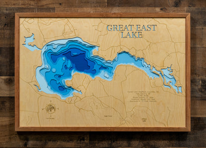 A framed wooden depth map of Great East Lake, featuring layered blue and cyan water contours on a light natural wood background, mounted on a dark rustic wood plank wall.