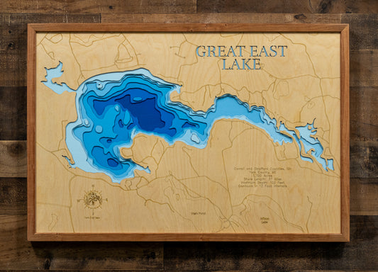 A framed wooden depth map of Great East Lake, featuring layered blue and cyan water contours on a light natural wood background, mounted on a dark rustic wood plank wall.