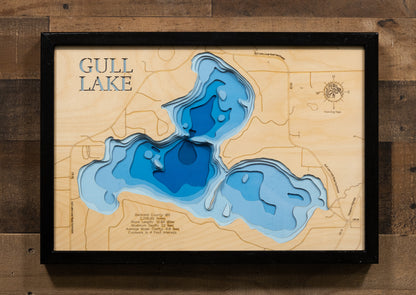 A laser-cut, layered wooden map of Gull Lake in Beltrami County, Minnesota. The distinct shape of this natural lake, with its 11.5-mile shoreline, is clearly visible within the forested landscape of northern Minnesota. The varying depths of the lake, reaching a maximum of 23 feet, are represented by different layers of wood, illustrating its impressive underwater topography.