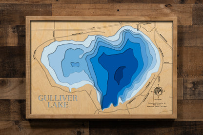 A precision laser-cut, multi-layered wooden map of Gulliver Lake in Schoolcraft County, Michigan — an Upper Peninsula lake draining to Lake Michigan just miles from the Seul Choix Point Lighthouse. The natural wood top layer captures the lake's shoreline in fine detail, while a light-to-dark blue gradient conveys its 28-foot depth. A handcrafted statement piece for any Michigan UP cabin, Great Lakes home, or outdoor enthusiast's wall.