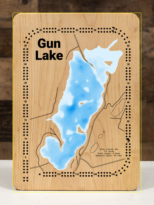 A meticulously detailed, laser-cut, multi-layered wooden topographical map of Gun Lake in Aitkin County, Minnesota, showcasing the 712-acre surface with intricate depth contours from diverse vegetated areas to the 44-foot maximum depth. The natural wood top layer frames nine miles of shoreline with abundant aquatic vegetation and the public boat access, while graduated blue layers create a striking visual depth gradient.