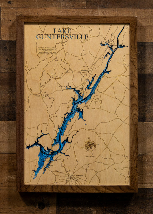 A laser-cut, layered wooden map of Lake Guntersville, located in Marshall, Jackson, DeKalb, and Marion Counties, Alabama. The expansive and intricate shape of the reservoir, stretching along the Tennessee River, is clearly visible within the northeastern Alabama landscape. The varying depths of the lake, reaching a maximum of 45 feet, are represented by different layers of wood, illustrating the underwater topography of this major Alabama water body.